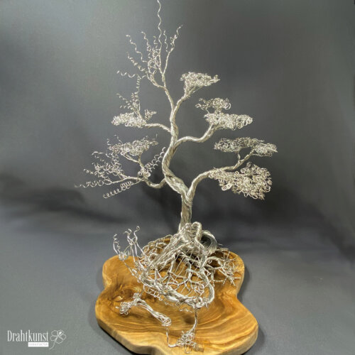 Saiten des Lebens: ein aus silberfarbenem Aluminiumdraht hergestellter Drahtbaum, der auf einer Teakholz-Baumscheibe thront