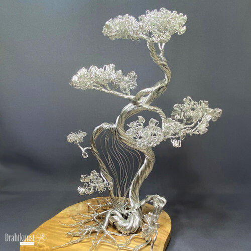 Klang der Stille: ein aus silberfarbenem Aluminiumdraht hergestellter Drahtbaum, der auf einer Teakholz-Baumscheibe thront