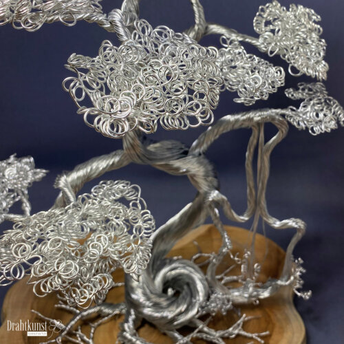 Melodie der Stärke: ein aus silberfarbenem Aluminiumdraht hergestellter Drahtbaum, der auf einer Teakholz-Baumscheibe thront